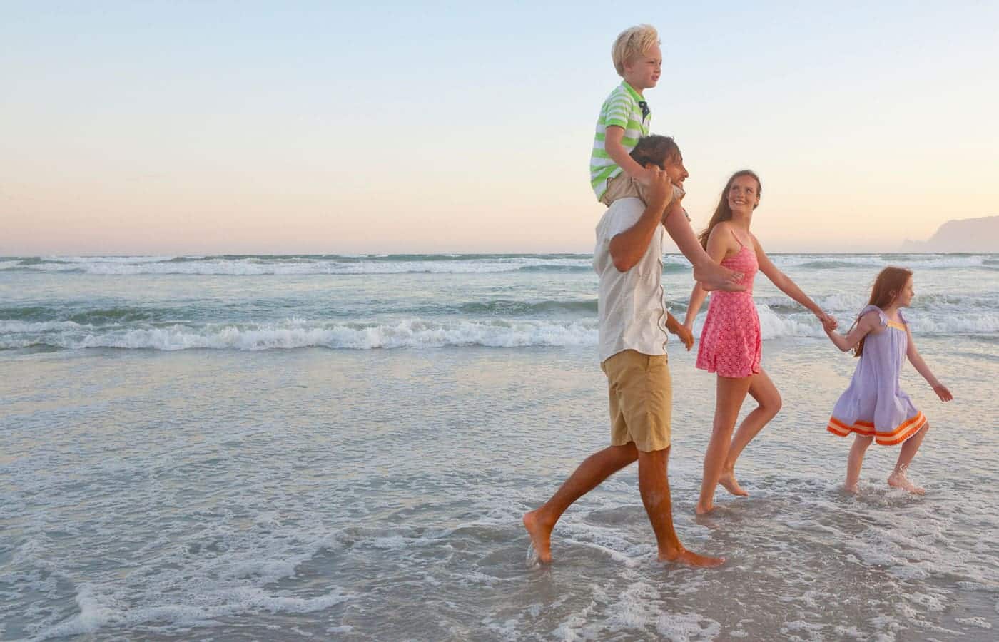 A woman serves breakfast to two smiling children and a man at a kitchen table set with pastries, oranges, berries, and glasses of orange juice.